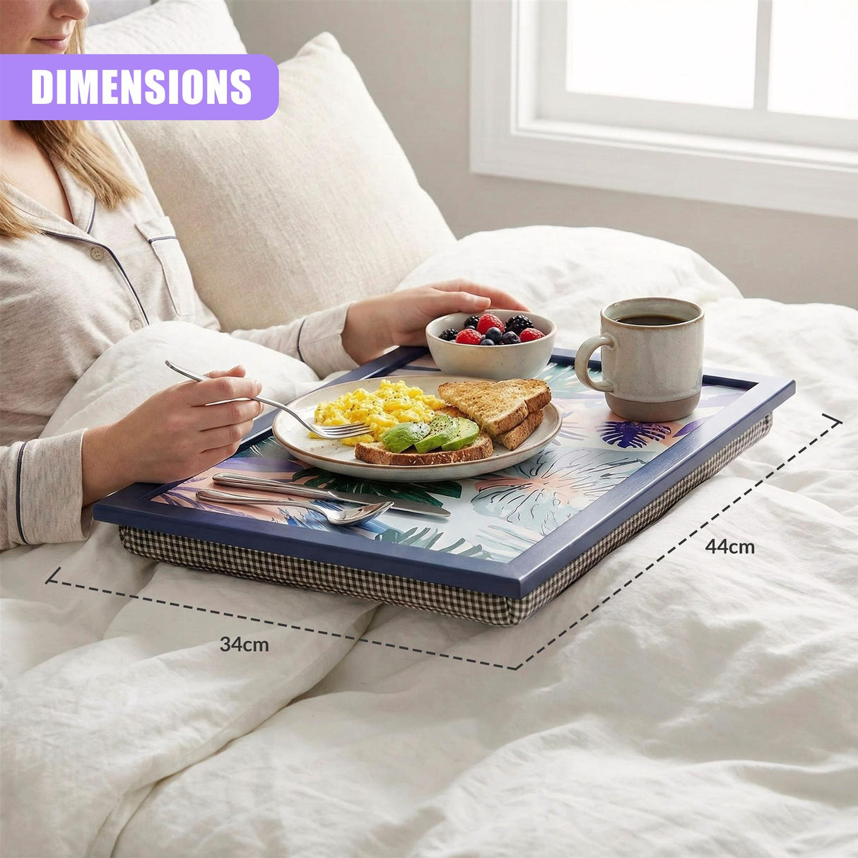 A woman in bed, holding a tray with a breakfast meal, including toast, eggs, and fruit, on a colorful, tropical-patterned tray with a blue frame, on a white bed with a white comforter. - UKBuyZone