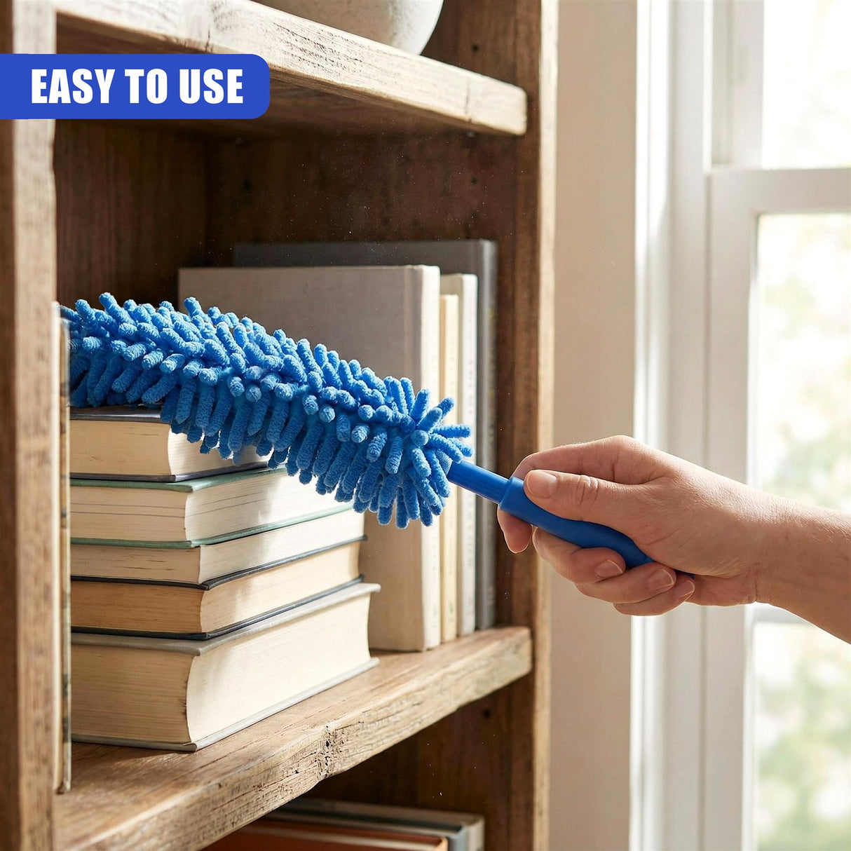 A person uses a blue, extendable duster to clean a wooden bookshelf stacked with books.