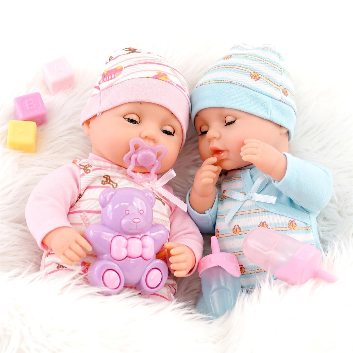 Two twin baby dolls in colorful outfits and hats, surrounded by accessories and a purple teddy bear.