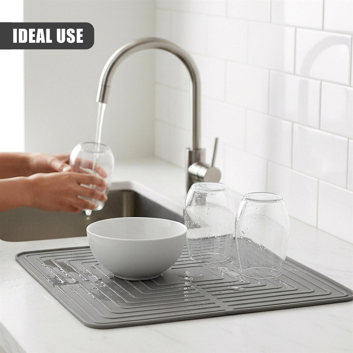 A draining mat holds several wet glasses and a bowl near a kitchen sink faucet.