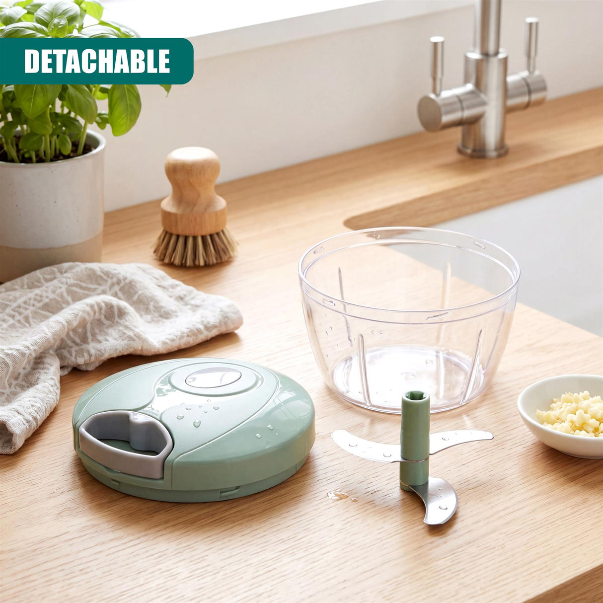 Mint green manual chopper base, removable metal blade, clear glass bowl, and small bowl of chopped ingredients.