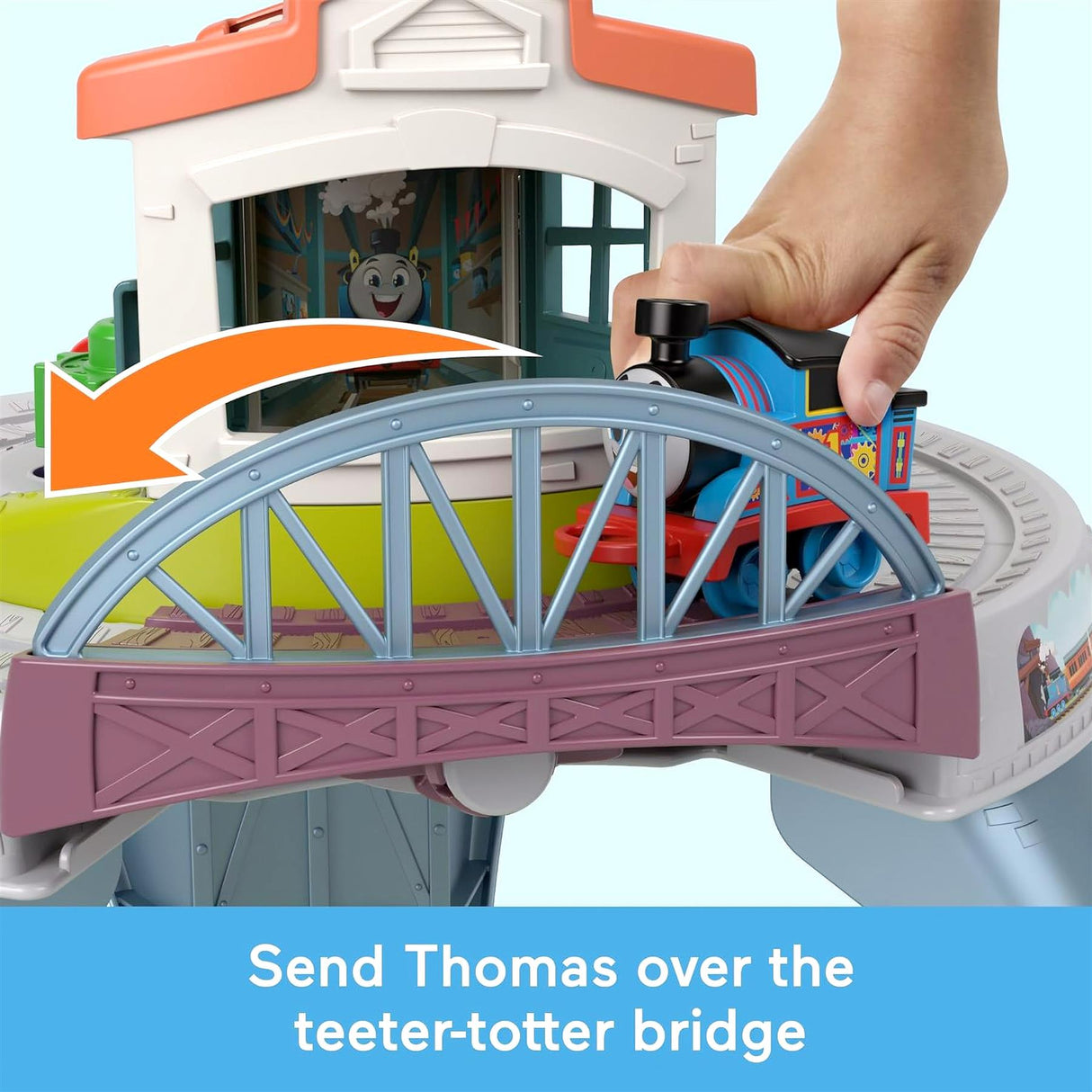 A hand guides a toy train across a bridge connecting sections of the play table.