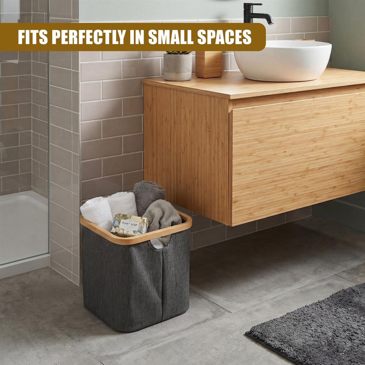 A gray fabric laundry hamper sits on the floor, holding folded towels and clothes next to a wood vanity.