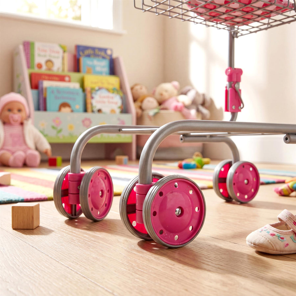 Pink caster wheels attached to a metal frame support a kids doll shopping trolley.