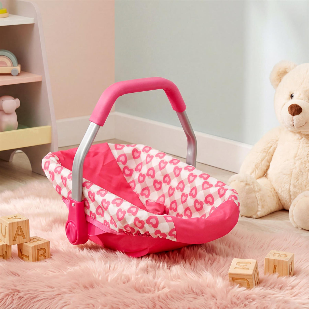 Pink baby play car seat with a heart pattern lining and curved carrying handle.