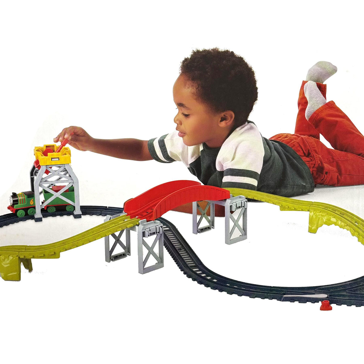 A young boy uses a toy train track set with a loading ramp and cargo drop feature.