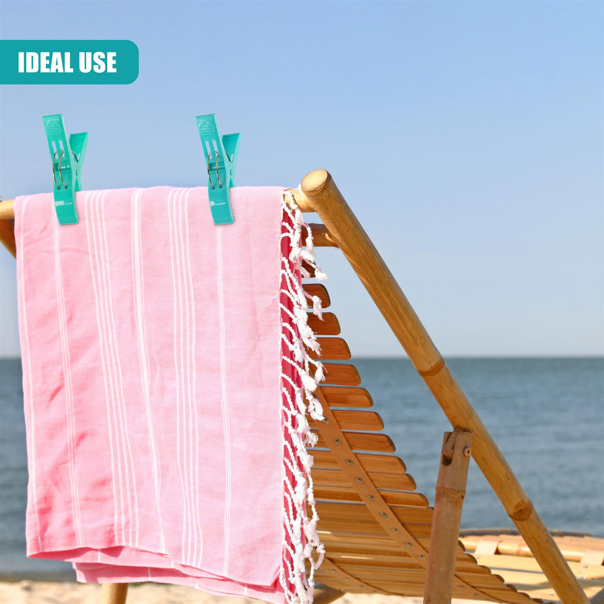Two teal clips hold a striped pink towel over a wooden beach chair against the ocean backdrop.