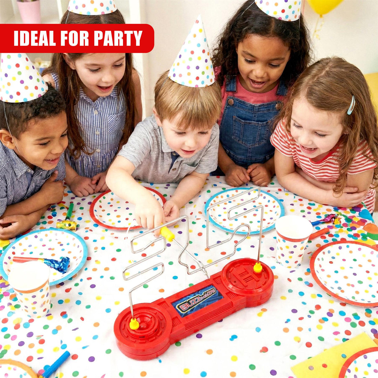 Children play with a red buzzer game set and coils on a table covered in colorful confetti.