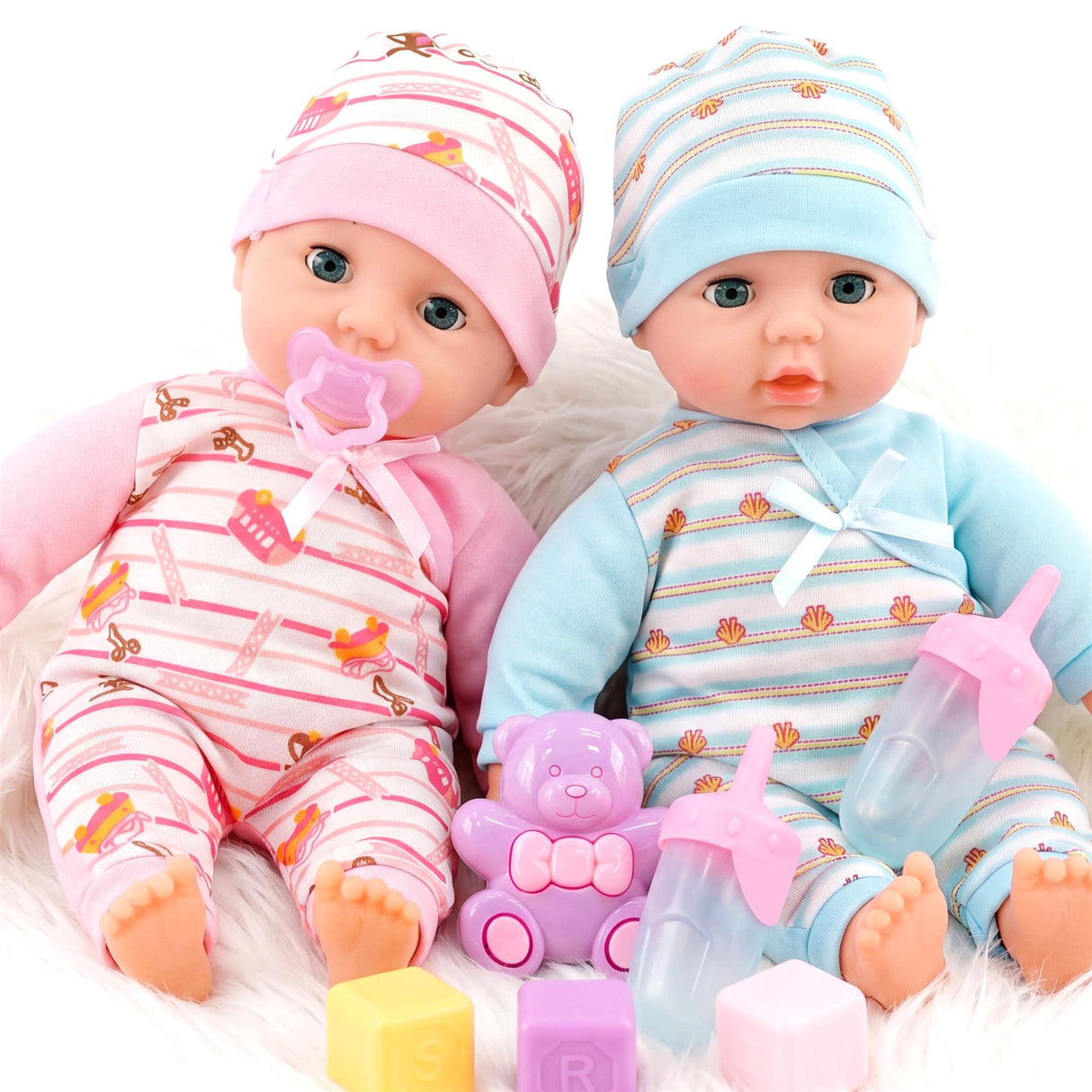 Two dolls in striped outfits sit with accessories, including a purple bear and blue and pink bottles.