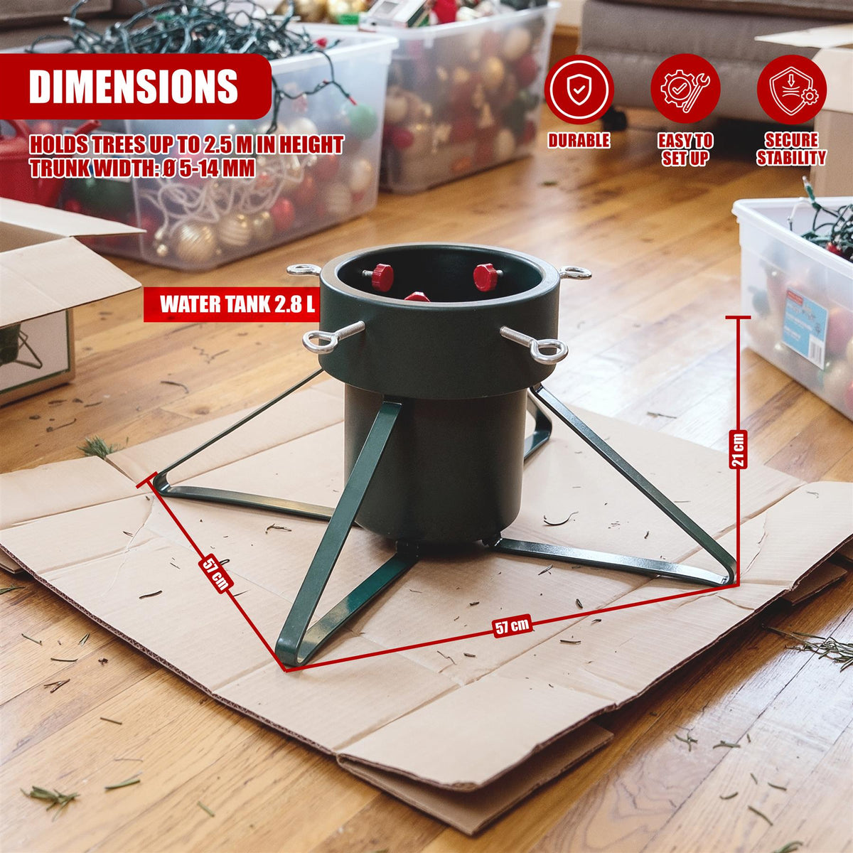 A green metal Christmas tree stand on a wooden floor, surrounded by storage boxes and cardboard packaging