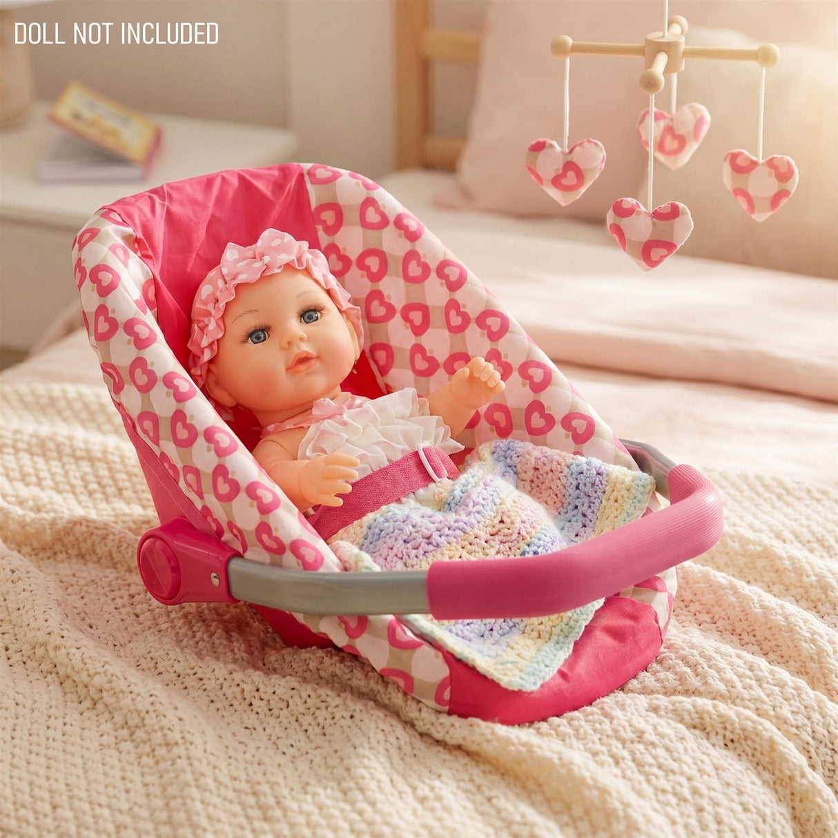 Plush, heart-patterned baby carrier with pink and gray handles resting on soft white bedding.