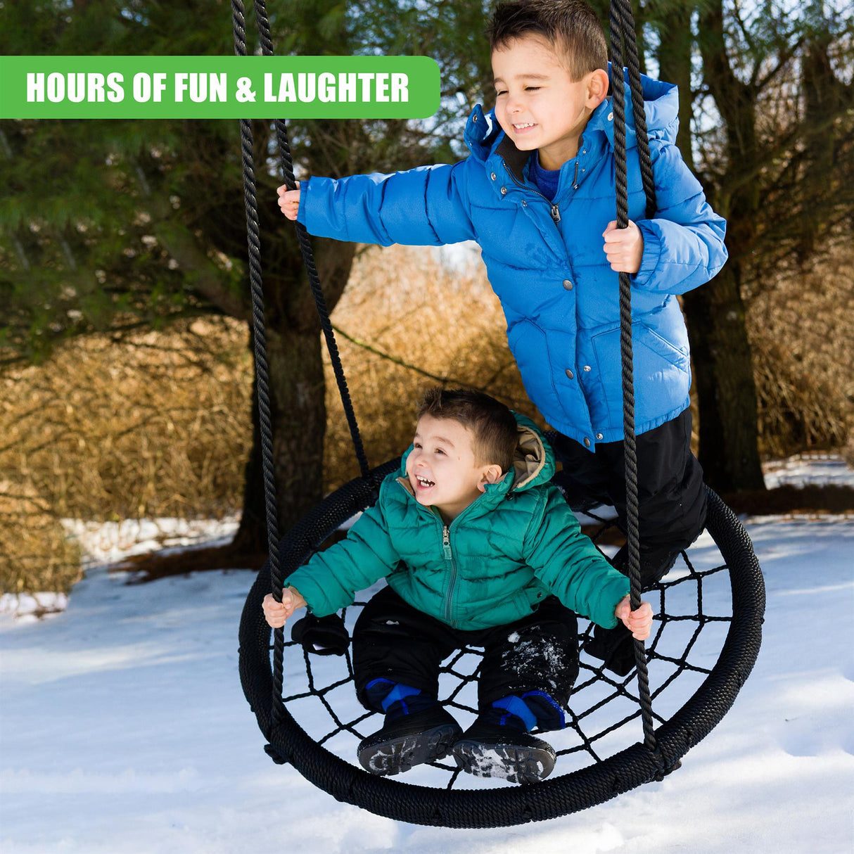 Two boys swing on a black nest swing outside on a sunny day.