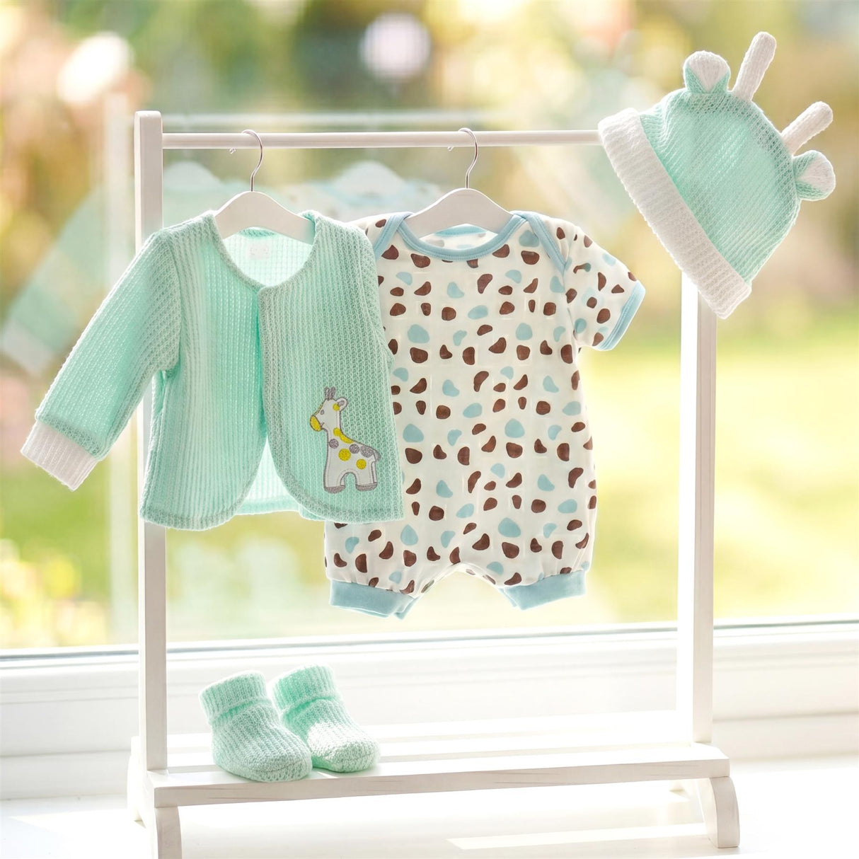 Mint green jacket, patterned romper, hat, and socks are displayed on a white clothing rack.