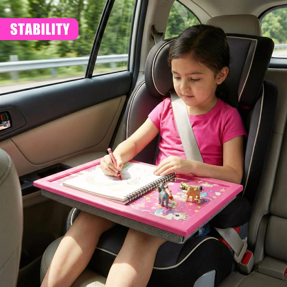 Child drawing on a pink lap tray decorated with a rainbow unicorn and small toys.