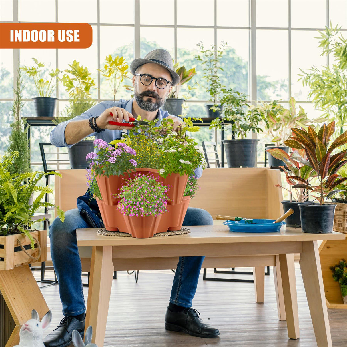 "A man tending to a collection of potted plants, including a strawberry planter and a rabbit in a wooden crate on a table, possibly in a plant shop or greenhouse." - UKBuyZone