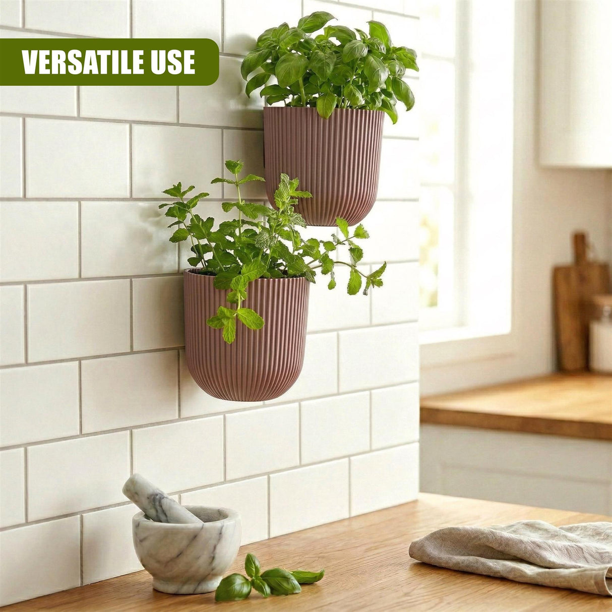 Two pink planters with green herbs hang on white subway tiles over a wooden counter.