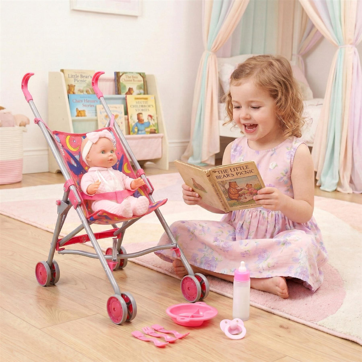 Pink baby doll in a stroller, feeding set, and a girl reading a book sit on the floor.