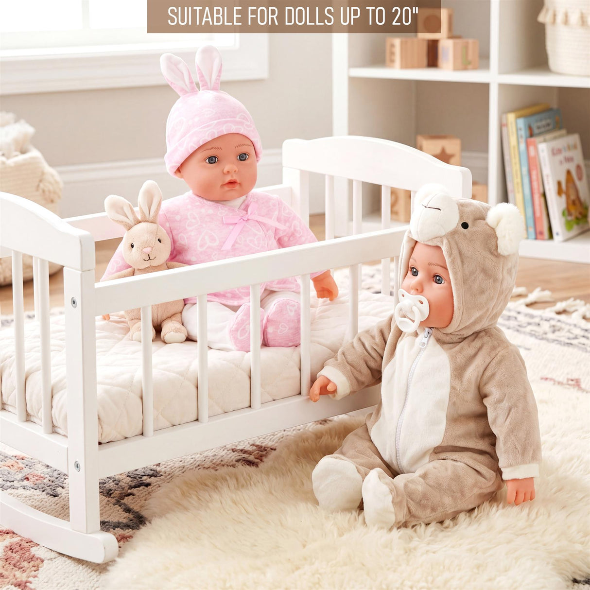 A doll in a pink bonnet sits in a crib next to a second doll wearing a bear-themed outfit.