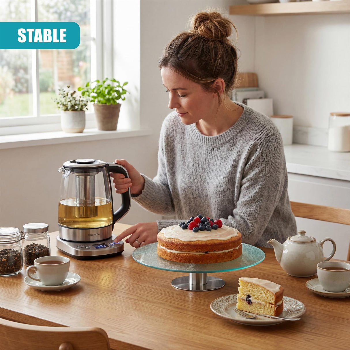 Round layer cake sits on a circular glass cake stand on a wooden kitchen counter.