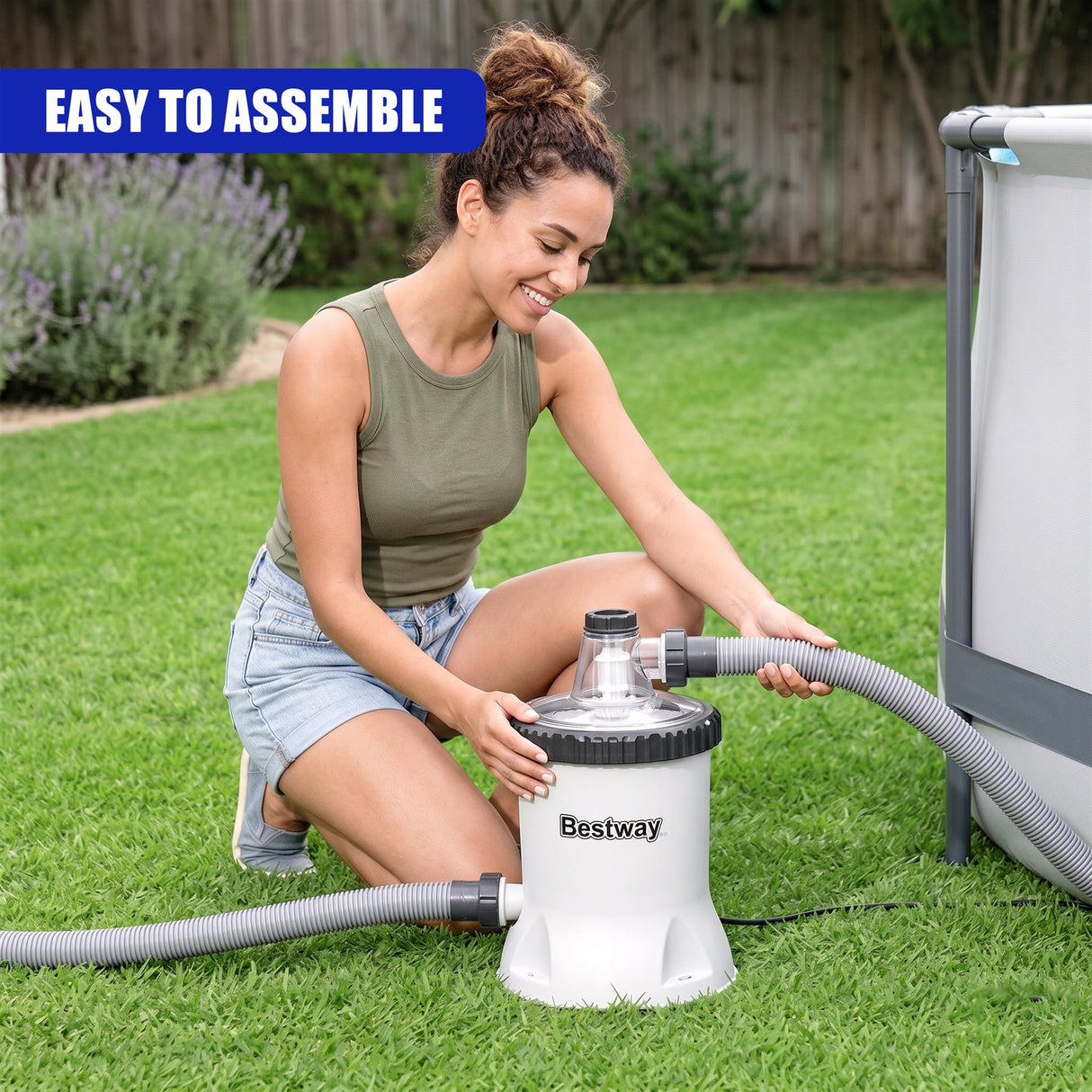 White circular pool filter pump unit with attached hoses resting on green grass.