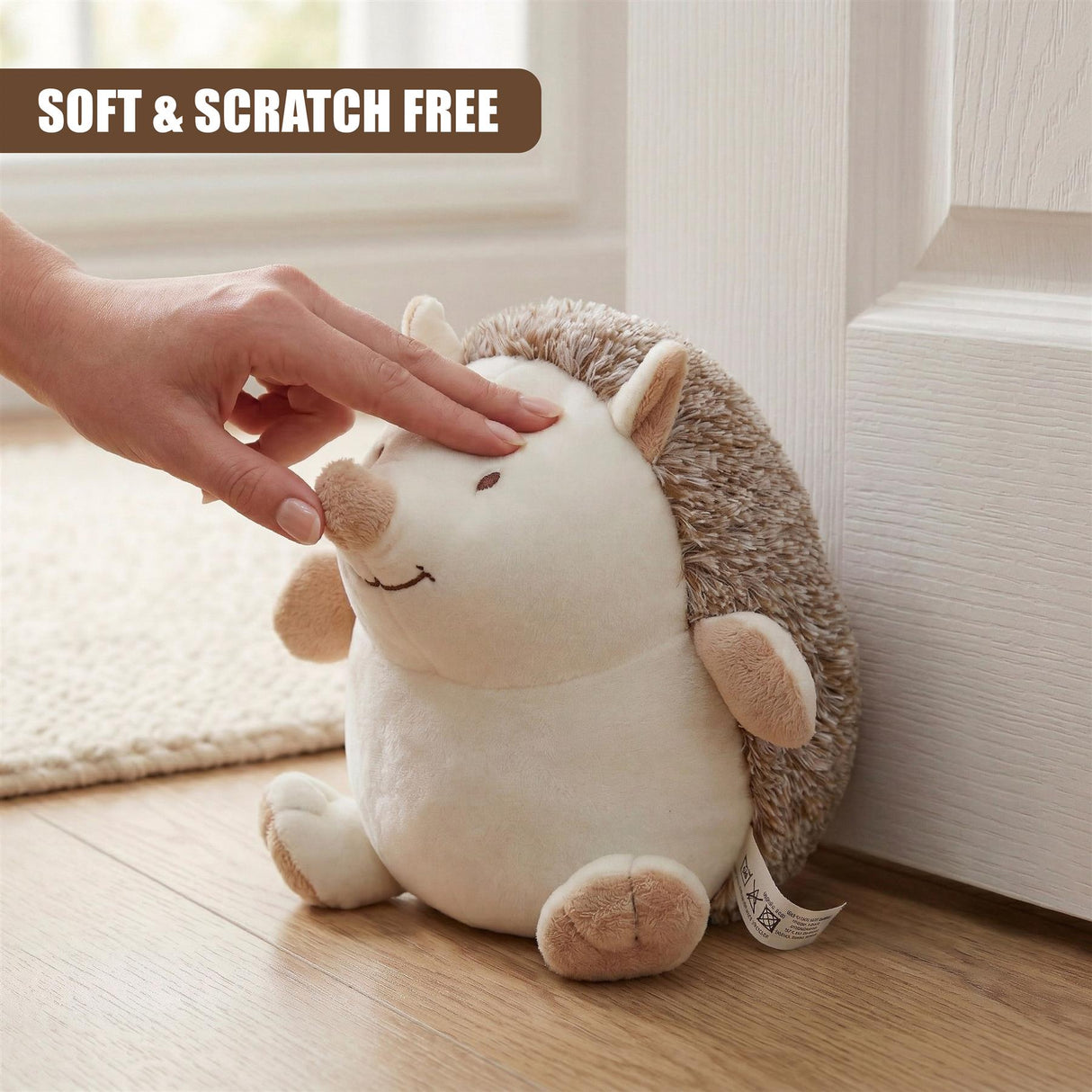 Hand petting a plush hedgehog door stop resting against white wood trim.