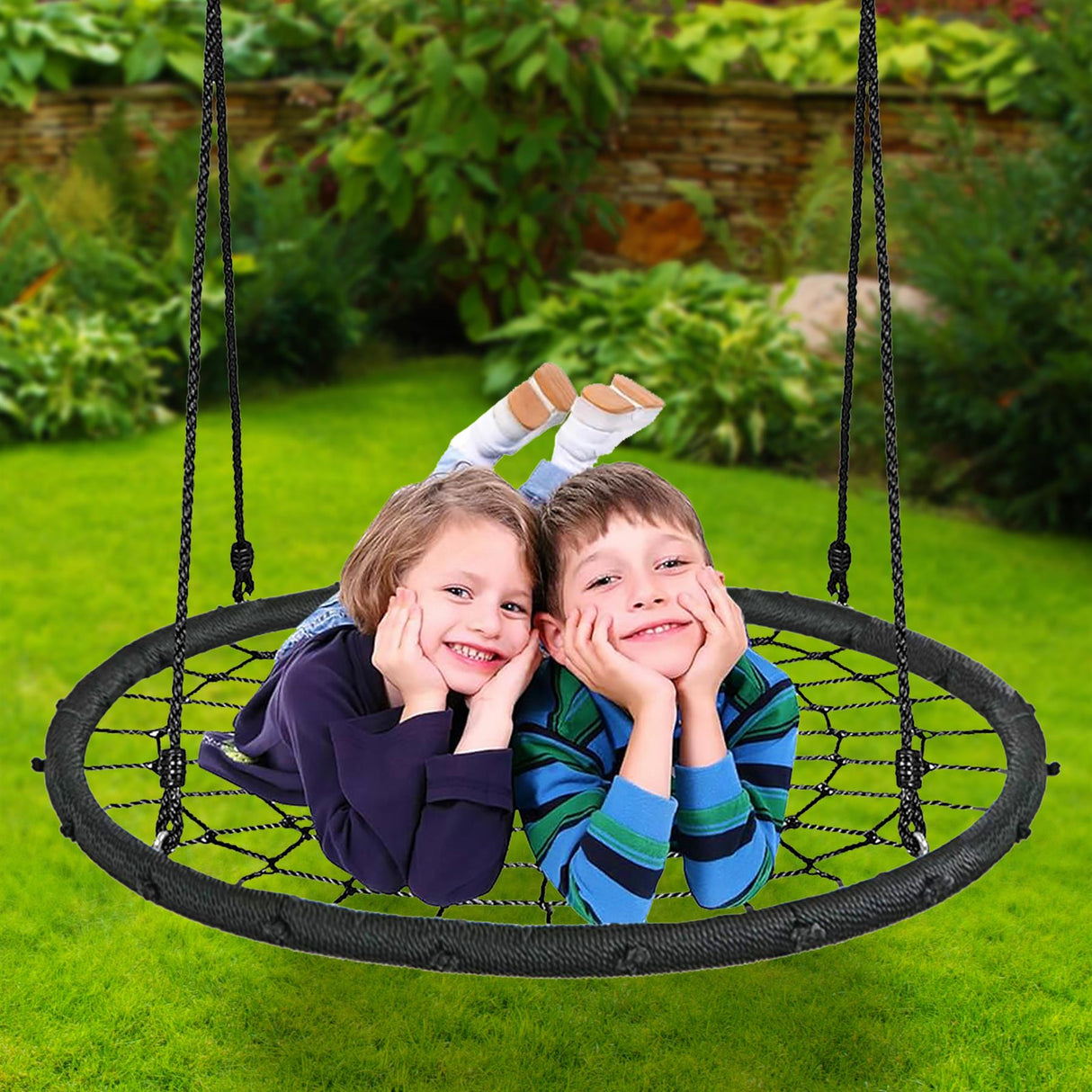 A black woven swing net holding two smiling children sitting in a lush outdoor garden setting.