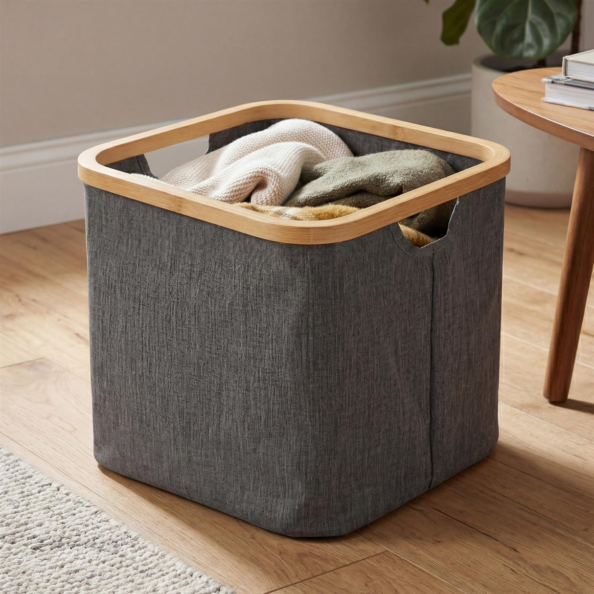 Gray fabric laundry hamper with a visible wooden rim, filled with folded white clothes.