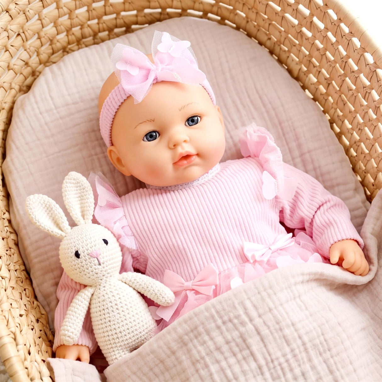 Baby doll wearing pink outfit and headband rests with a cream stuffed bunny in a basket.