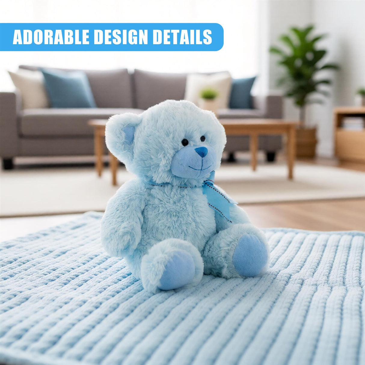 A plush, soft blue teddy bear sits on a light blue, textured blanket in a living room setting. The bear has a blue nose and a blue, embroidered collar. The background is blurred, with a couch, coffee table, and plant in the distance. - UKBuyZone