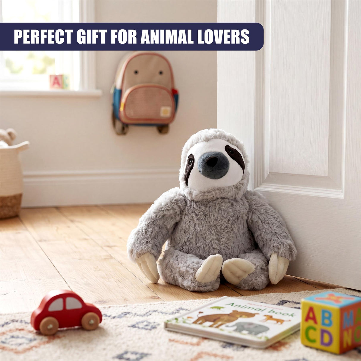 Stuffed gray sloth plush toy sits on a patterned rug near children's books and a doorway.