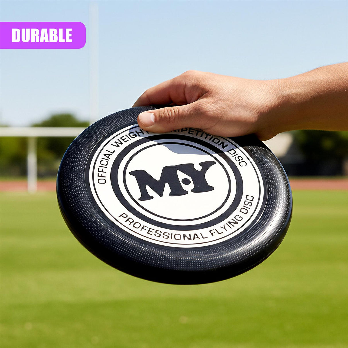 A hand holds a black official flying disc with white lettering and a circular logo.
