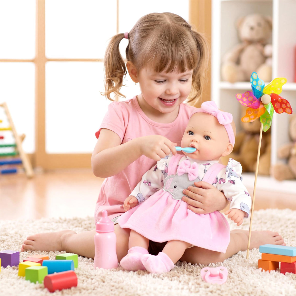 A little girl plays with a doll dressed in pink, surrounded by colored toy blocks and bottles.