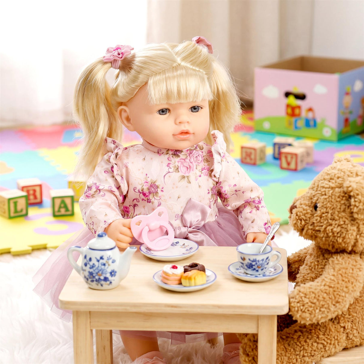 Blonde doll with pigtails sits at a table displaying a tea set, snack plate, and teddy bear.