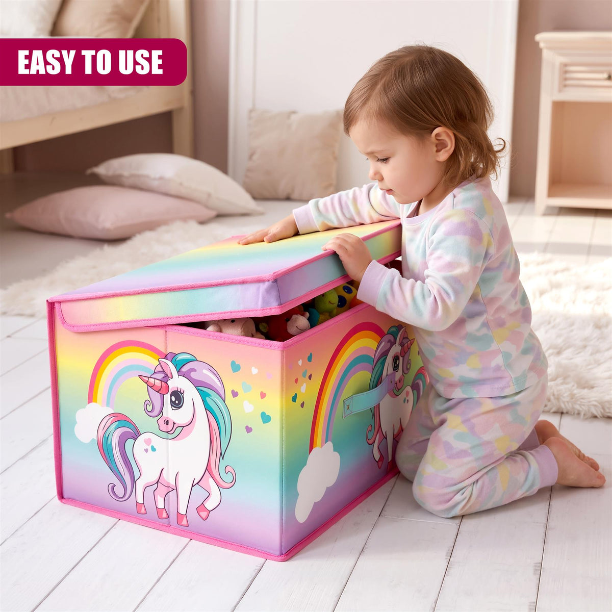 A child in a multi-coloured patterned onesie kneels on a white rug, opening a rainbow unicorn storage box filled with toys