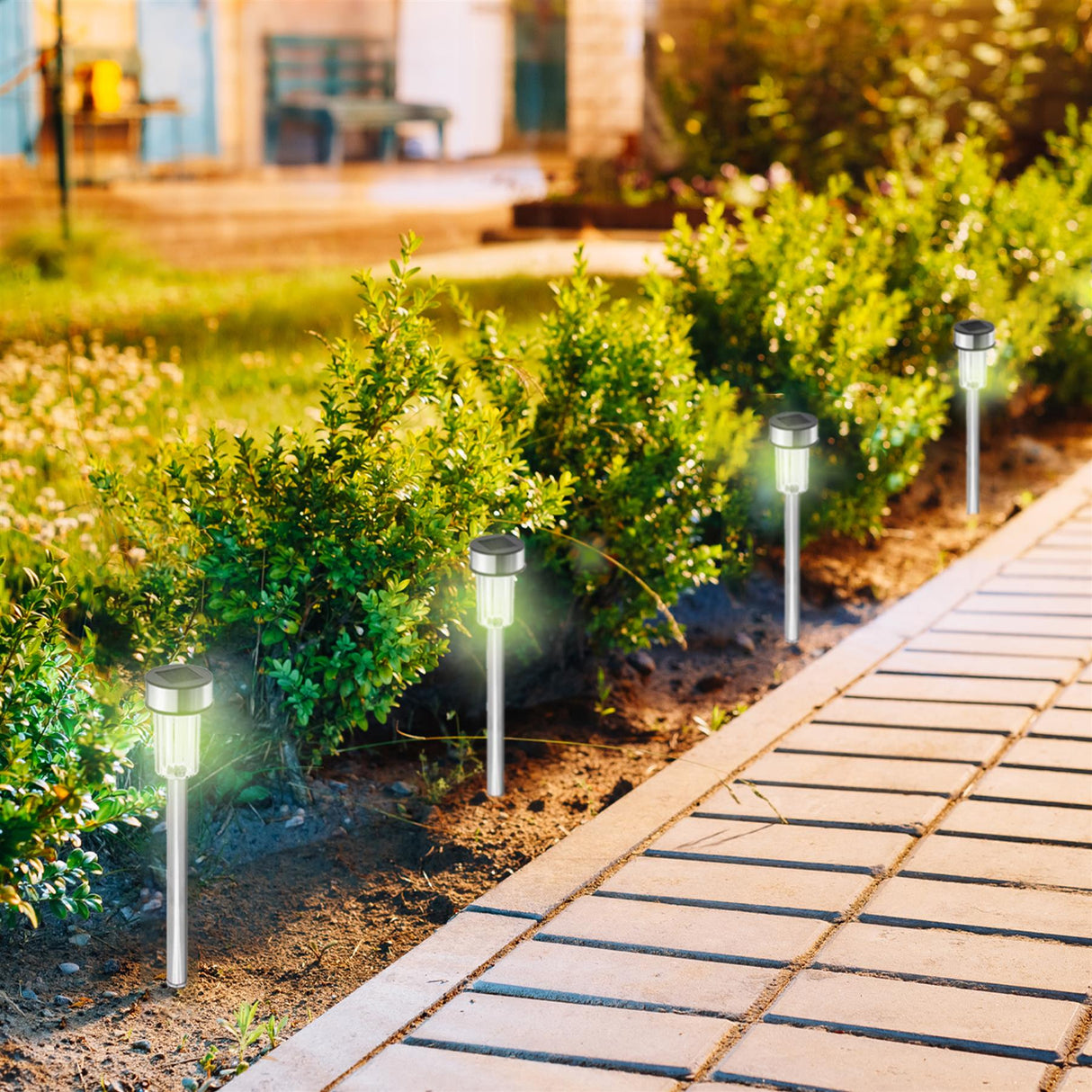 Modern solar path lights stand among dense green shrubs lining a structured patio walkway.