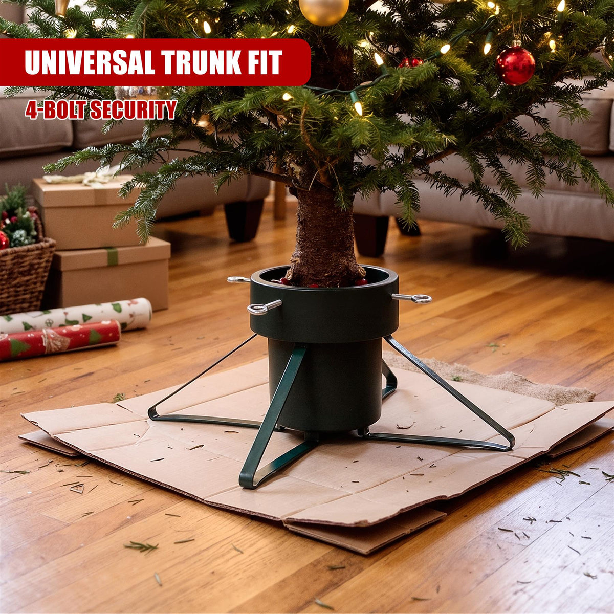 A green metal Christmas tree stand holding a decorated tree on a wooden floor with wrapping paper nearby