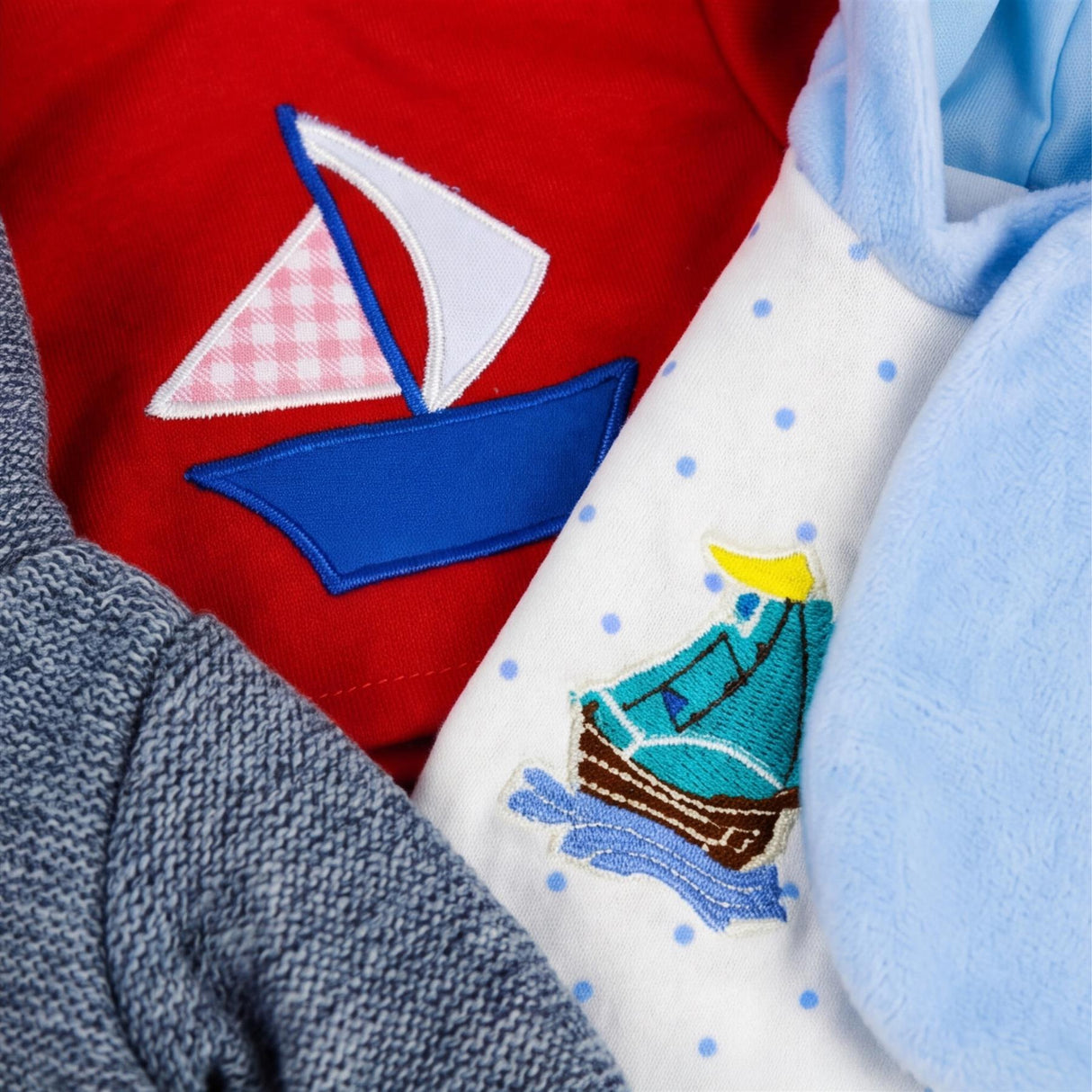 Gray knitted sweater, red baby outfit with a sailboat, and white outfit with blue boat graphic.