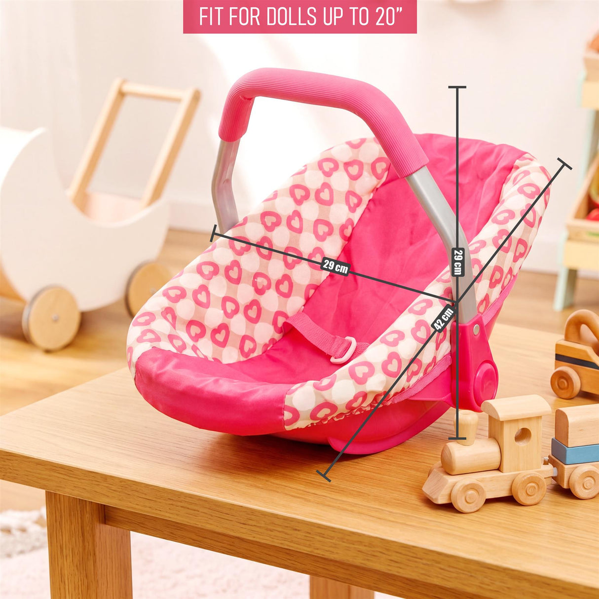 Pink and white patterned doll car seat with a handle placed on a light wooden table.