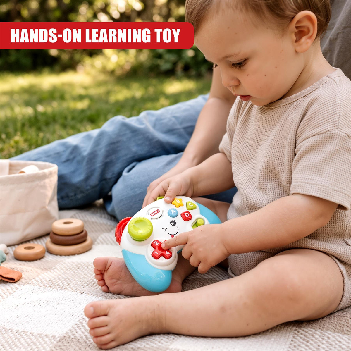 A baby wearing a beige top sits on a blanket outdoors, playing with a Game Controller Toy from The Magic Toy Shop