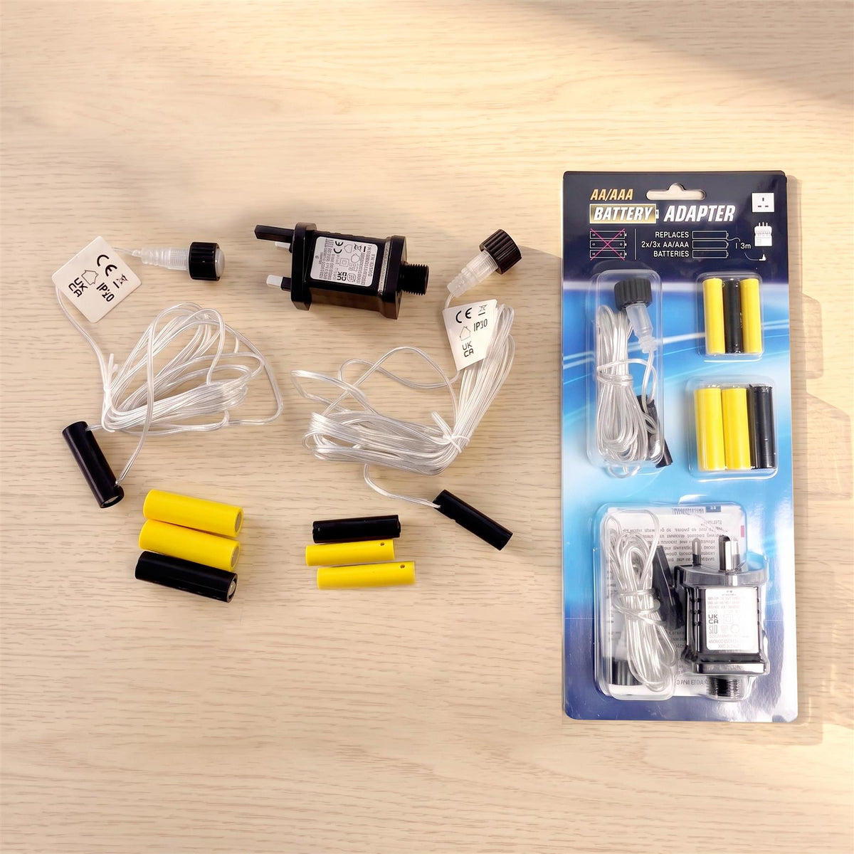 A flat lay of a Geezy battery eliminator kit on a light wood surface, showing loose components and the retail packaging