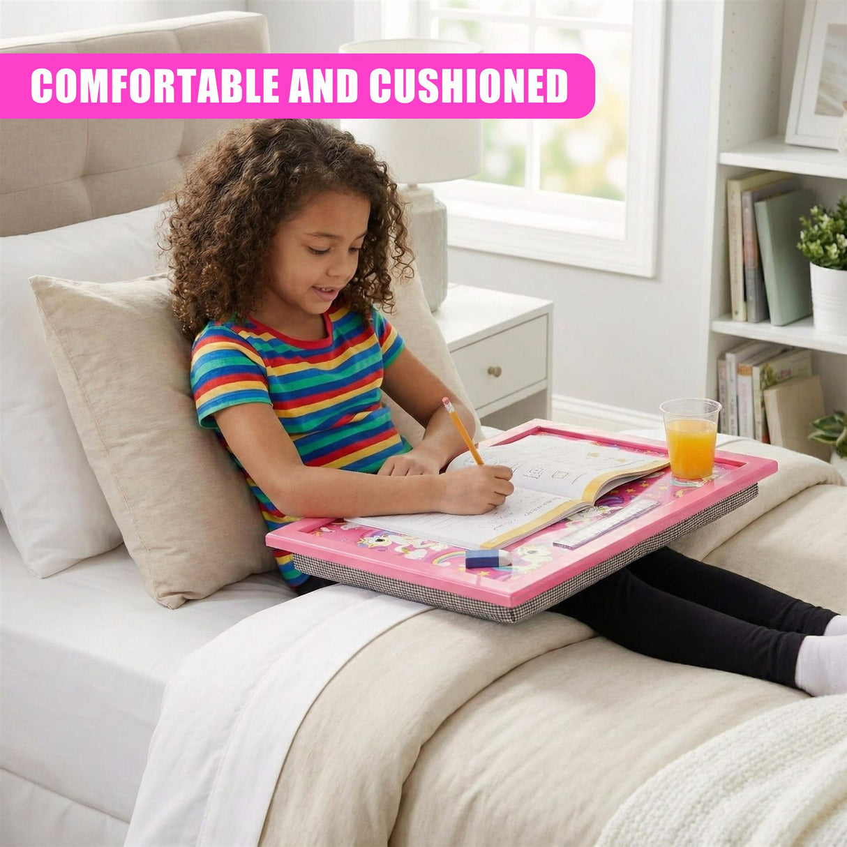 Young girl writing on a pink lap tray set up on a bed.