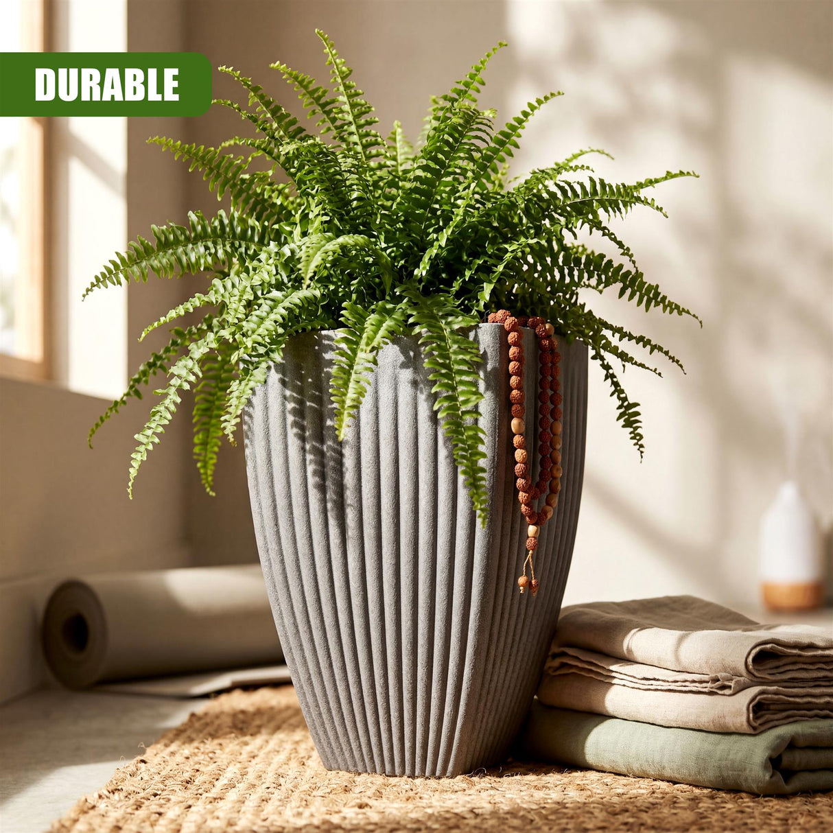 A tall, ribbed gray vase holds vibrant green fern plants and hanging wooden decorative beads.
