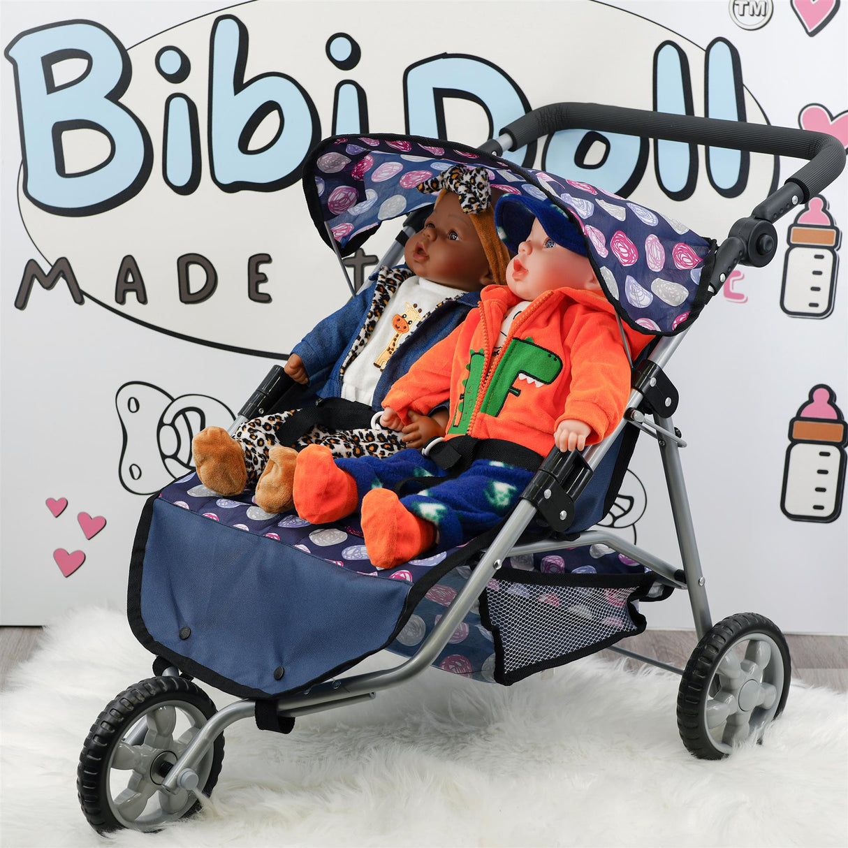 A blue twin doll stroller holds two seated dolls dressed in contrasting colored outfits.