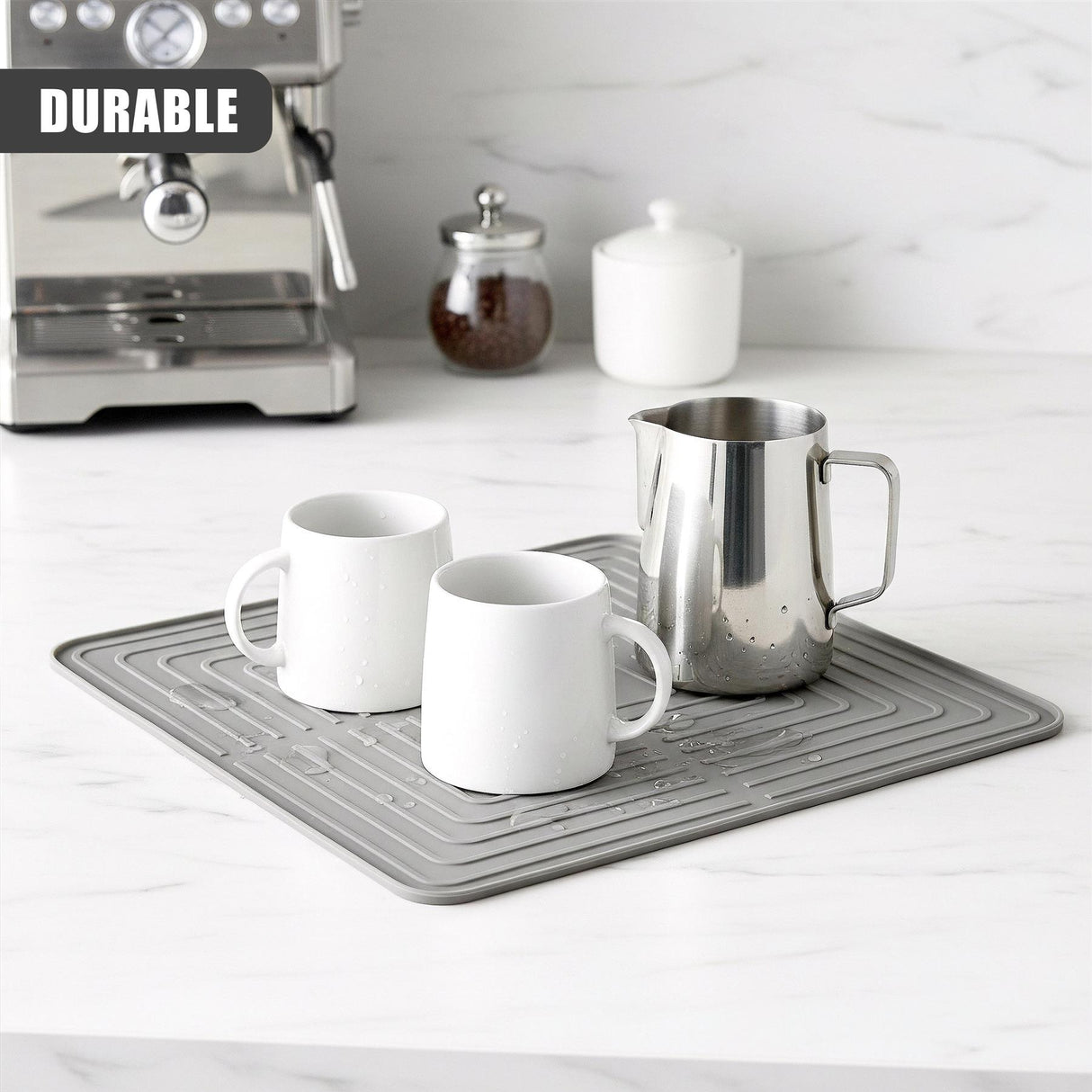 Gray perforated drying mat holding three white ceramic mugs and a stainless steel pitcher.