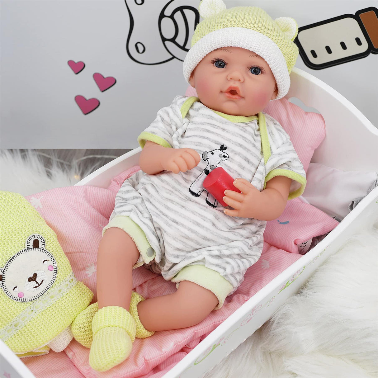 A baby doll wearing stripes and a hat rests in a pink wooden cradle with a yellow toy.
