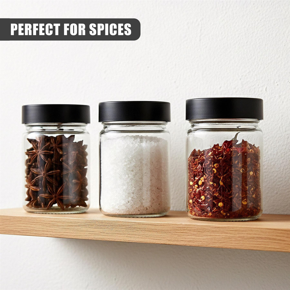 Three clear glass spice jars on a wood shelf, holding visible spices like star anise, white powder, and red blends.