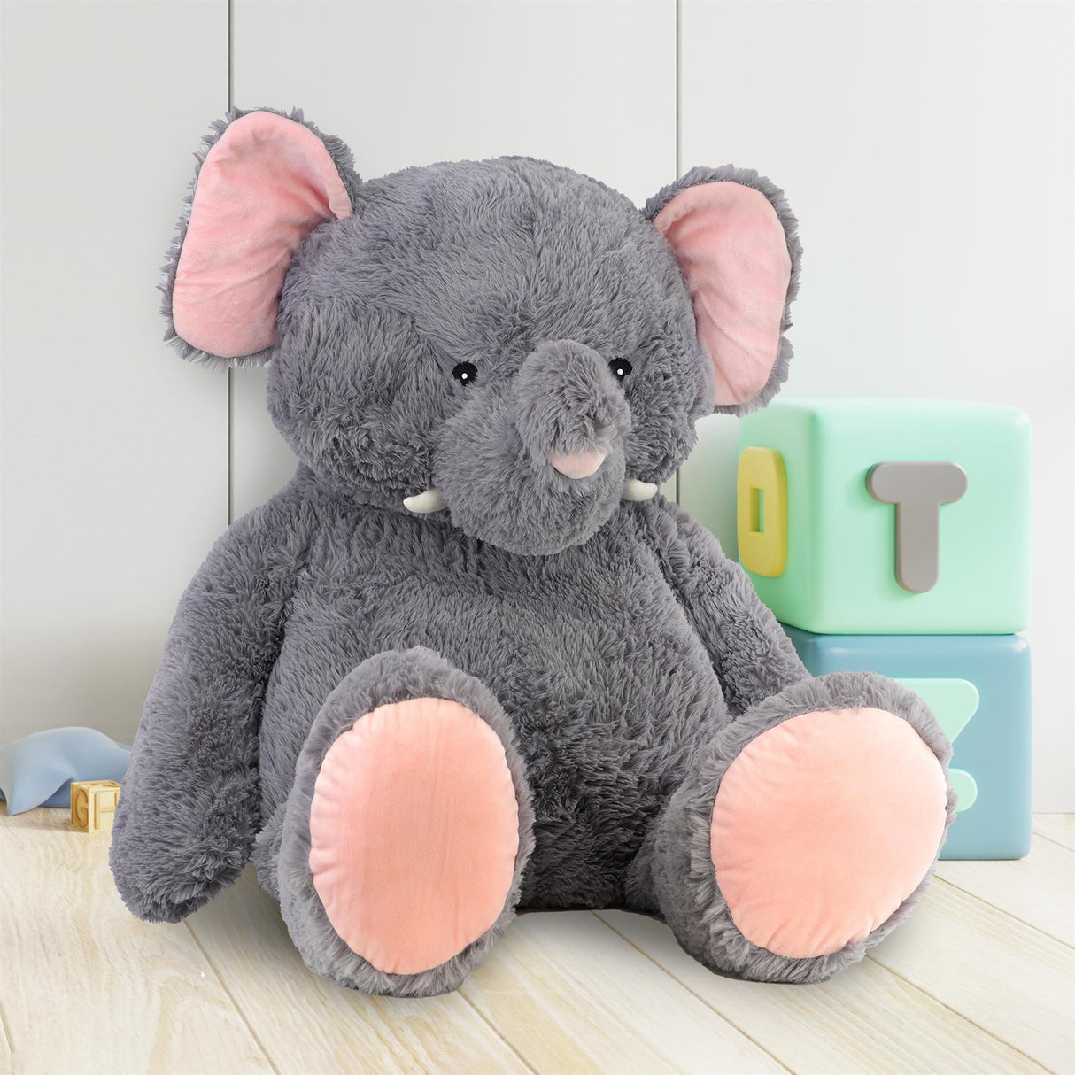 Plush gray elephant toy with pink feet is positioned beside stacked colorful alphabet letter blocks.
