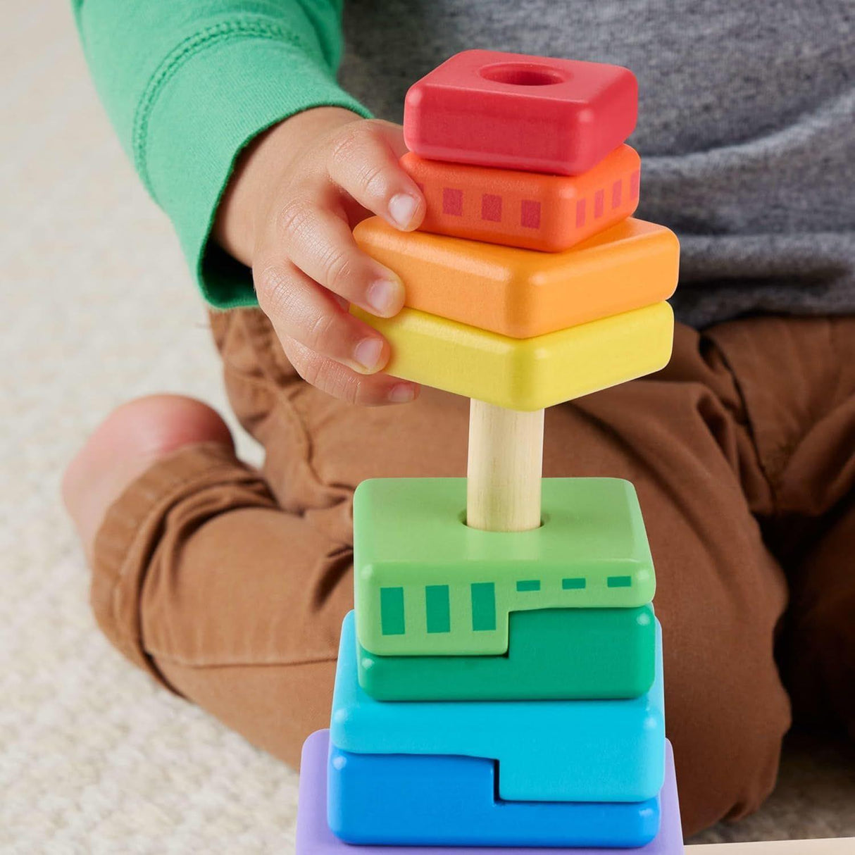 Colorful wooden stacking shapes are assembled in a column, held by a child's hands.