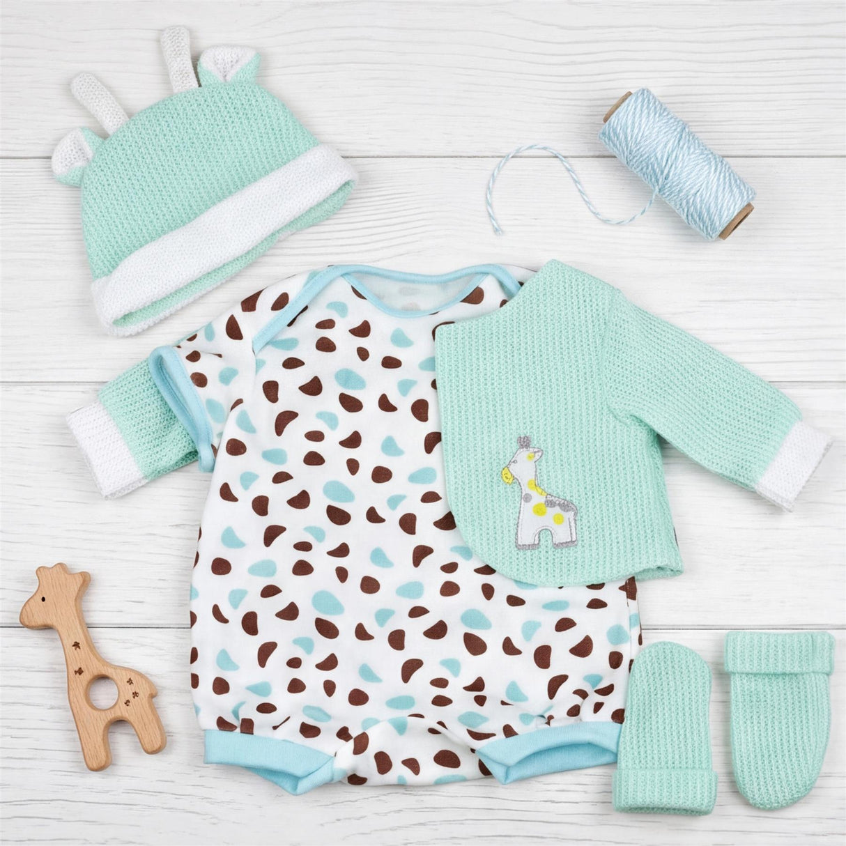 Set of baby clothes including spotted bodysuit, mint jacket, crocheted hat, booties, and wooden toy.