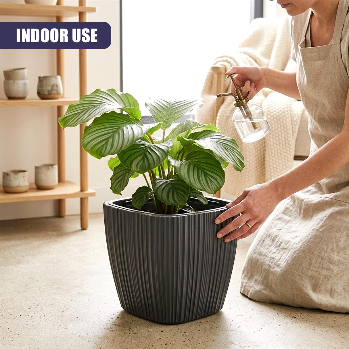 A woman waters a leafy houseplant in a black, fluted, vertical potted container.